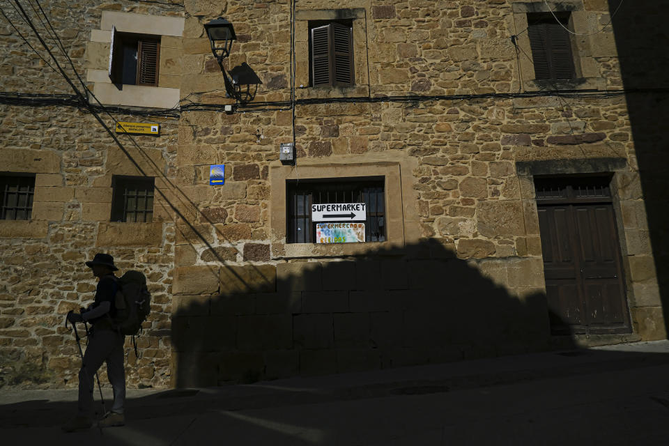 A pilgrim walks along ancient street during a stage of "Camino de Santiago" or St. James Way in Cirauqui, northern Spain, Tuesday, May 31, 2022. Over centuries, villages with magnificent artwork were built along the Camino de Santiago, a 500-mile pilgrimage route crossing Spain. Today, Camino travelers are saving those towns from disappearing, rescuing the economy and vitality of hamlets that were steadily losing jobs and population. “The Camino is life,” say villagers along the route. (AP Photo/Alvaro Barrientos)