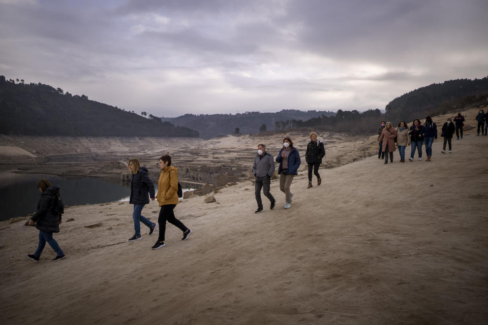 Local residents walk to visit the old village of Aceredo emerged due to drought at the Lindoso reservoir, in northwestern Spain, Saturday, Feb. 12, 2022. Roofs emerging from the waters have become a common scene every summer at the Lindoso reservoir, in northwestern Spain. In especially dry years, parts of the old village of Aceredo, submerged three decades ago when a hydropower dam flooded the valley, would appear. But never before had the skeleton of the village emerged in its entirety, in the middle of the usually wet winter season. (AP Photo/Emilio Morenatti)