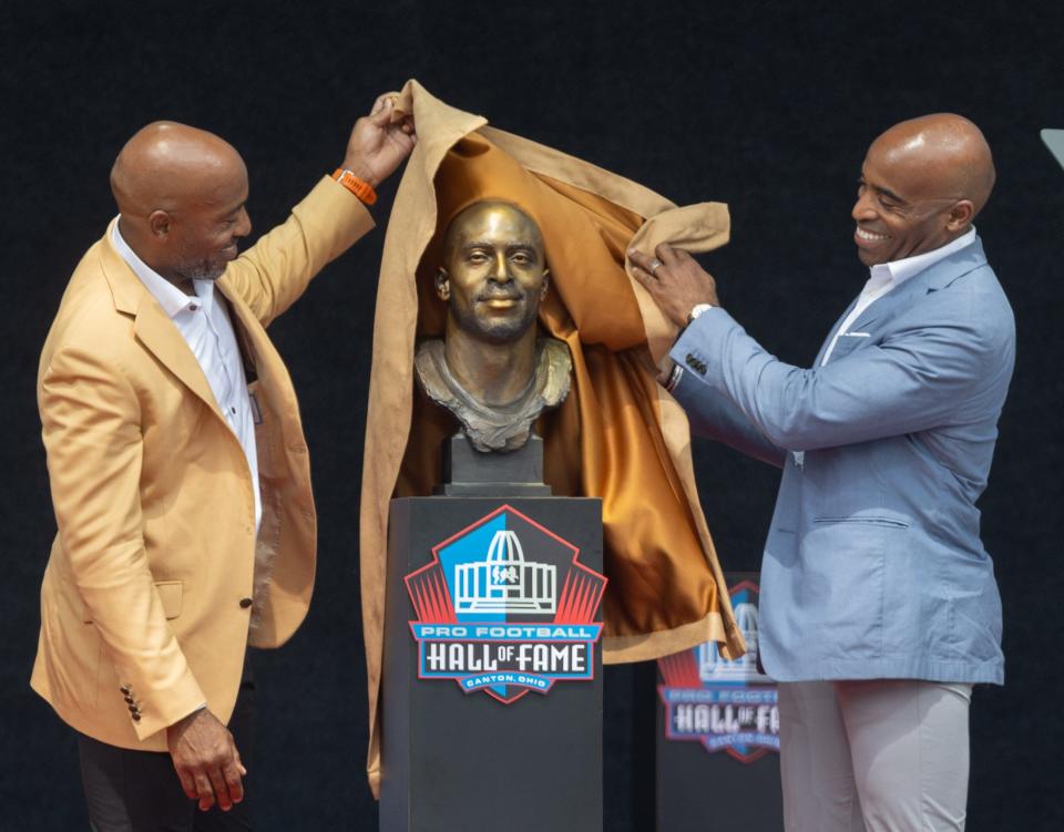 Rondé Barber, left, and his twin brother, Tiki, unveil Rondé’s bust during the Enshrinement on Saturday.