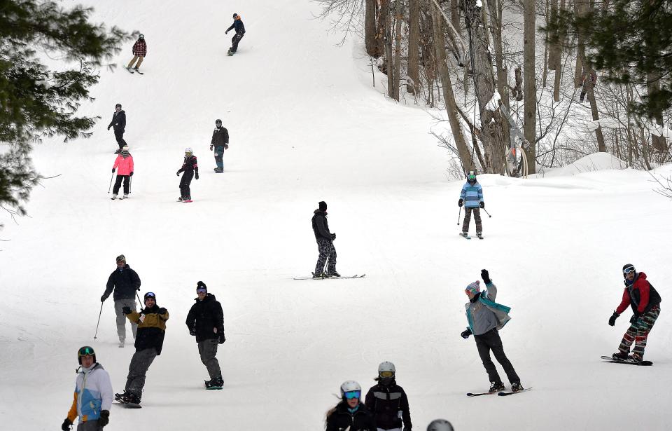 Skiers and snowboarders descend a slope at Peek'n Peak Resort on Jan. 23, 2021, near Findley Lake, New York. Due to pandemic restrictions, the number of skiers on the slopes is reduced by 25%. Indoor areas are reduced to 50% capacity. 