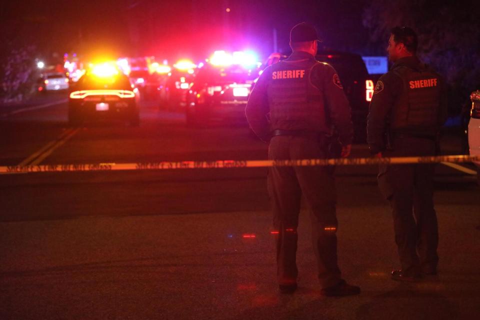 Sheriff's deputies stand before squad cars with lights flashing