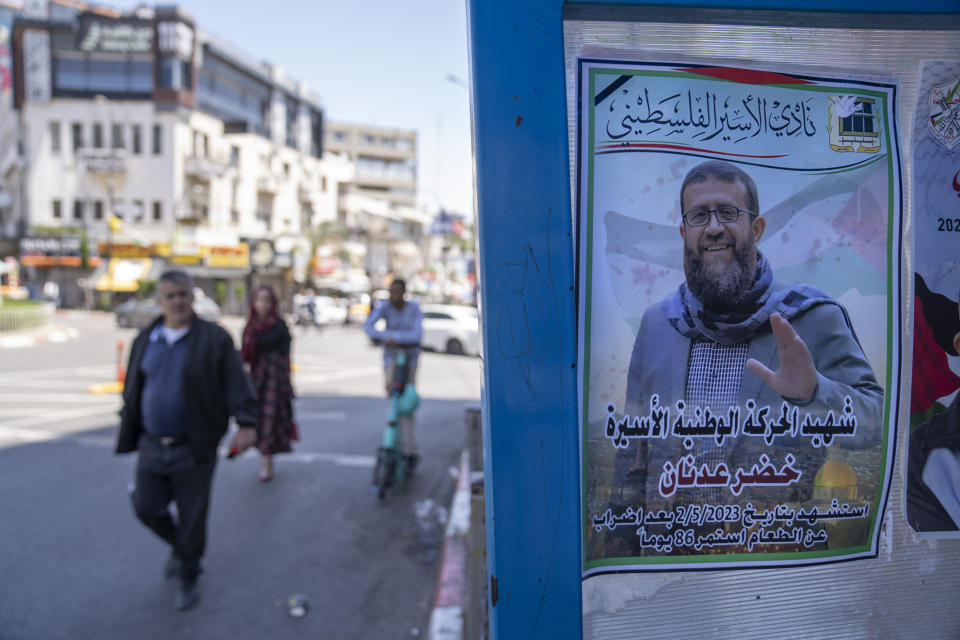 Palestinians walk past a poster of Khader Adnan, a leader in the militant Islamic Jihad group, and Arabic that reads "the Martyr of the prisoners national movement, a martyr after a 86 days of hunger strike," in the West Bank city of Ramallah Tuesday, May 2, 2023. A high-profile Palestinian prisoner died in Israeli custody on Tuesday after a nearly three-month-long hunger strike, Israel's prison service announced. (AP Photo/Nasser Nasser)