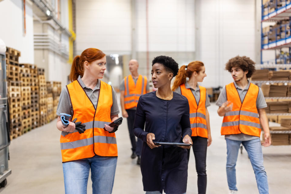 Warehouse manager discussing delivery schedules with a female worker. Warehouse supervisor walking and talking with dispatch worker.