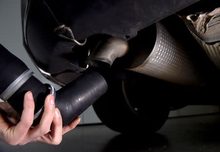 A worker attaches rubber tubing to the exhaust of a car to enable emissions testing to take place on the vehicle, at 'Emissions Analytics' in west London. REUTERS/Hannah McKay