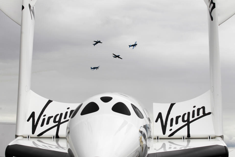 Seen in between the wings of the Virgin Galatica VSS Enterprise, the Blades aerobatics team fly in display during Farnborough International Airshow, Farnborough, England, Monday, July 9, 2012. (AP Photo/Sang Tan)