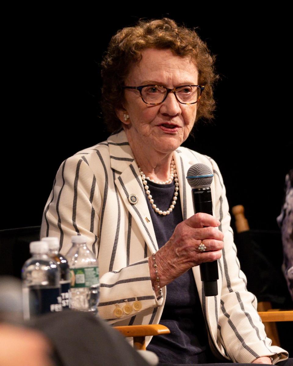 ann burgess holding a microphone while speaking as part of a panel