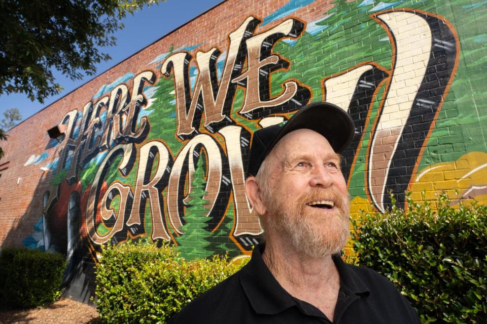 A bearded man smiles in front of a mural.