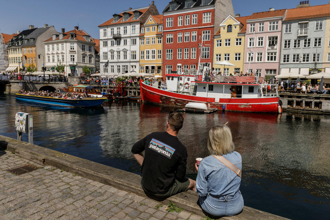 COPENHAGEN, DENMARK - 2024/05/25: Tourists are sitting on the canal embankment in the Nyhavn area ñ a popular tourist spot known for its colorful historic houses, bars, restaurants, and boats. Copenhagen ranks fourth in the world in the Mercer 2023 Quality of Living Survey. A stable economy, excellent education services, and high social safety make it attractive for locals and tourists. Copenhagen is also one of the world's most expensive cities and a popular tourist destination. (Photo by Volha Shukaila/SOPA Images/LightRocket via Getty Images)