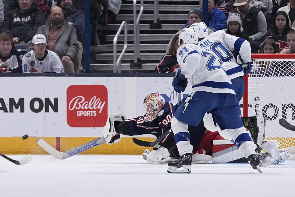 Columbus Blue Jackets goalie Elvis Merzlikins (90) flips the puck into the corner, away from Tampa Bay Lightning center Brayden Point (21) and left wing Nicholas Paul (20) during the second period of an NHL hockey game Thursday, Nov. 2, 2023, in Columbus, Ohio. (AP Photo/Sue Ogrocki)