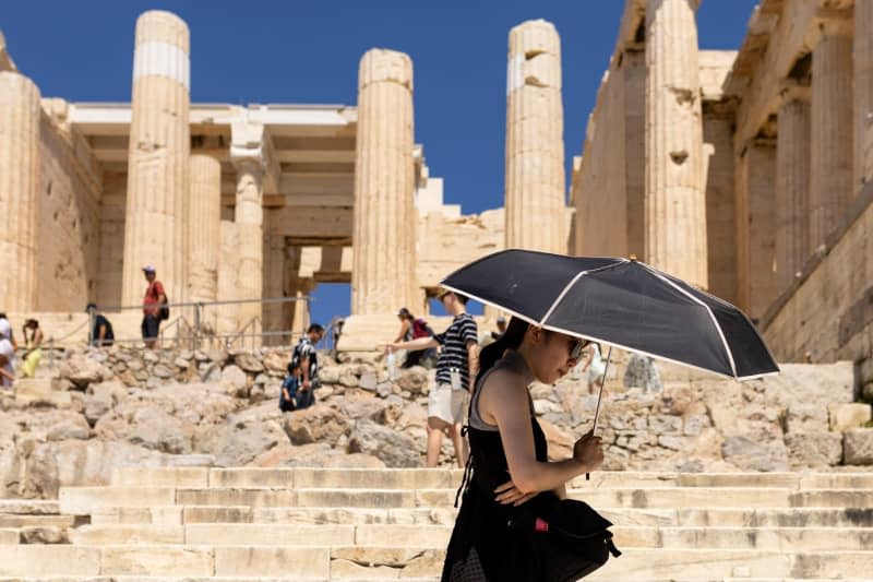 A tourist walks under an umbrella during their visit to the Acropolis in Athens. Greece has been hit by extreme heat particularly early this year. According to meteorologists, it has never been this hot since records began in early June as temperatures reached up to 40 degrees at times - and even higher in the blazing midday sun. Socrates Baltagiannis/dpa