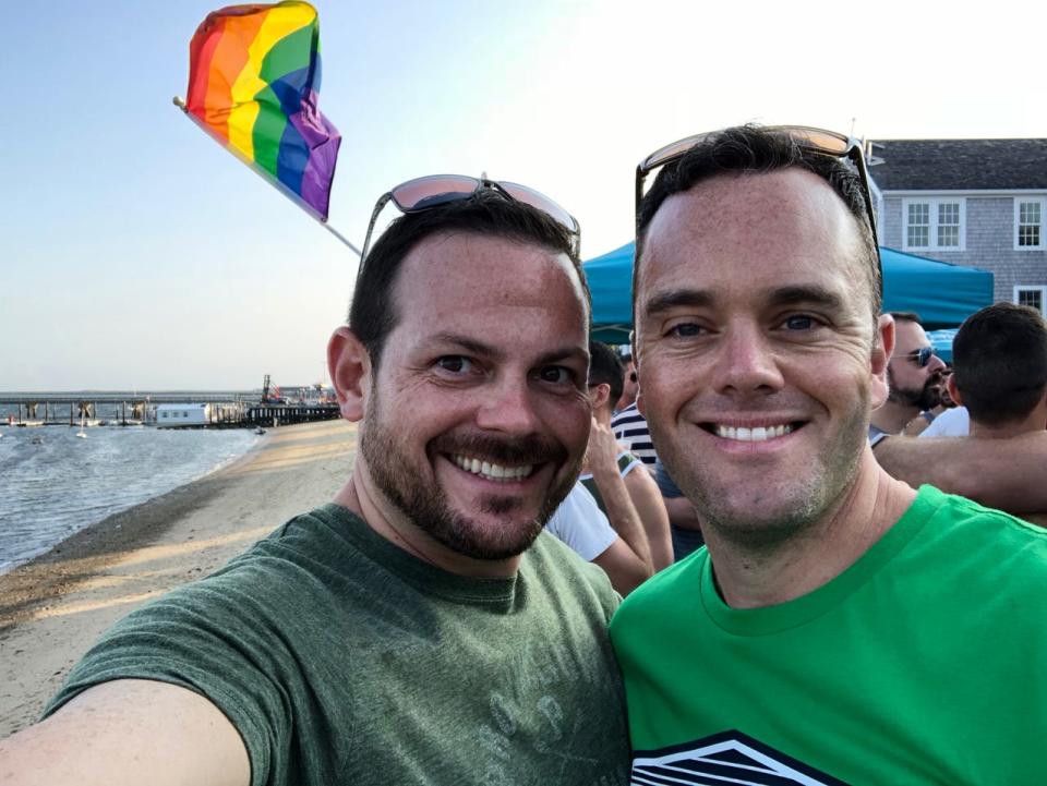 LeeMichael McLean and Bryan Furze pose in front of a Pride flag. During more than five years of harassment, about 30 pieces of mail with homophobic fake names on them were sent to the couple’s home in Milton, Massachusetts.