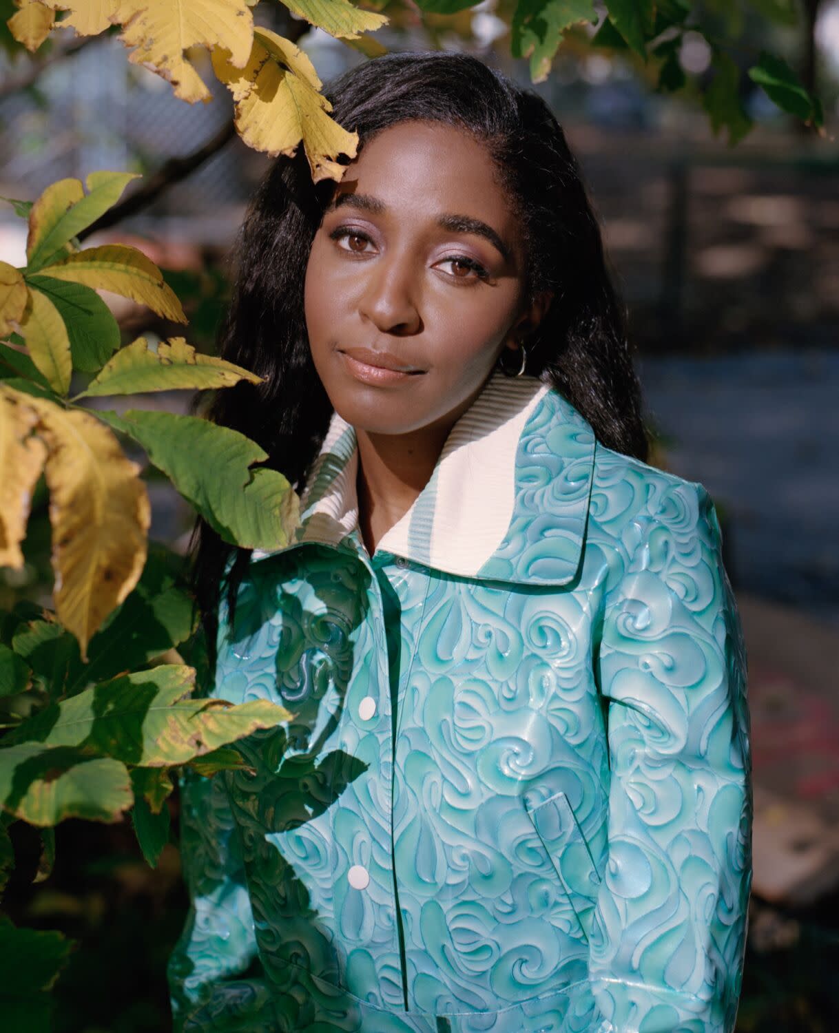 A woman stands next to greenery in a park and looks forward