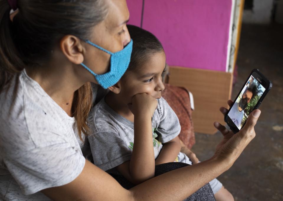 In this April 27, 2020 photo, Daniel sits in grandmother's lap in their apartment in Caracas, Venezuela, as they chat via a messenger service with his father Misael Cocho. After fleeing Venezuela along with millions of others amid the country's grueling humanitarian crisis, Cocho made his way by bus to Peru — where he got odd jobs and sent money home monthly to support his mother and his 5-year-old son. But just after Cocho landed his steadiest work so far in Lima, the new coronavirus cases skyrocketed. He lost his job. (AP Photo/Ariana Cubillos)