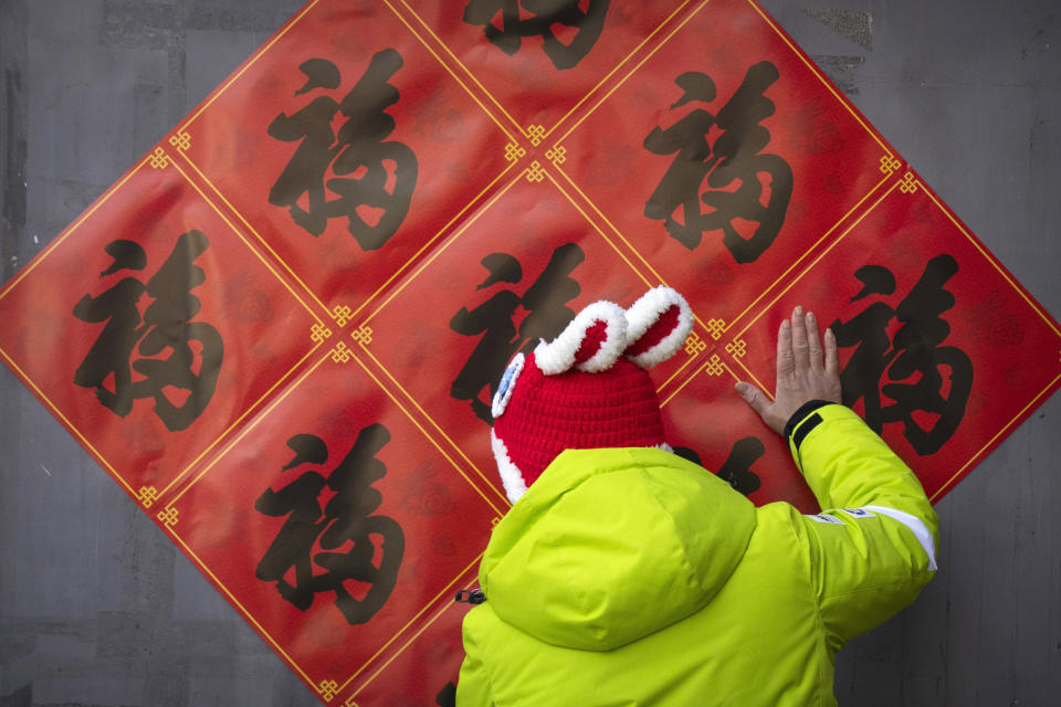 A woman uses her hand to smooth out decorations for the upcoming Lunar New Year that she put up on a wall at a tourist shopping street in Beijing, Saturday, Jan. 21, 2023. The Year of the Rabbit officially begins on Sunday. (AP Photo/Mark Schiefelbein)