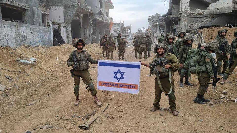 Two soldiers in Gaza hold an Israeli flag, altered to include an orange stripe and the words, in Hebrew: “Coming home!” - Social Media