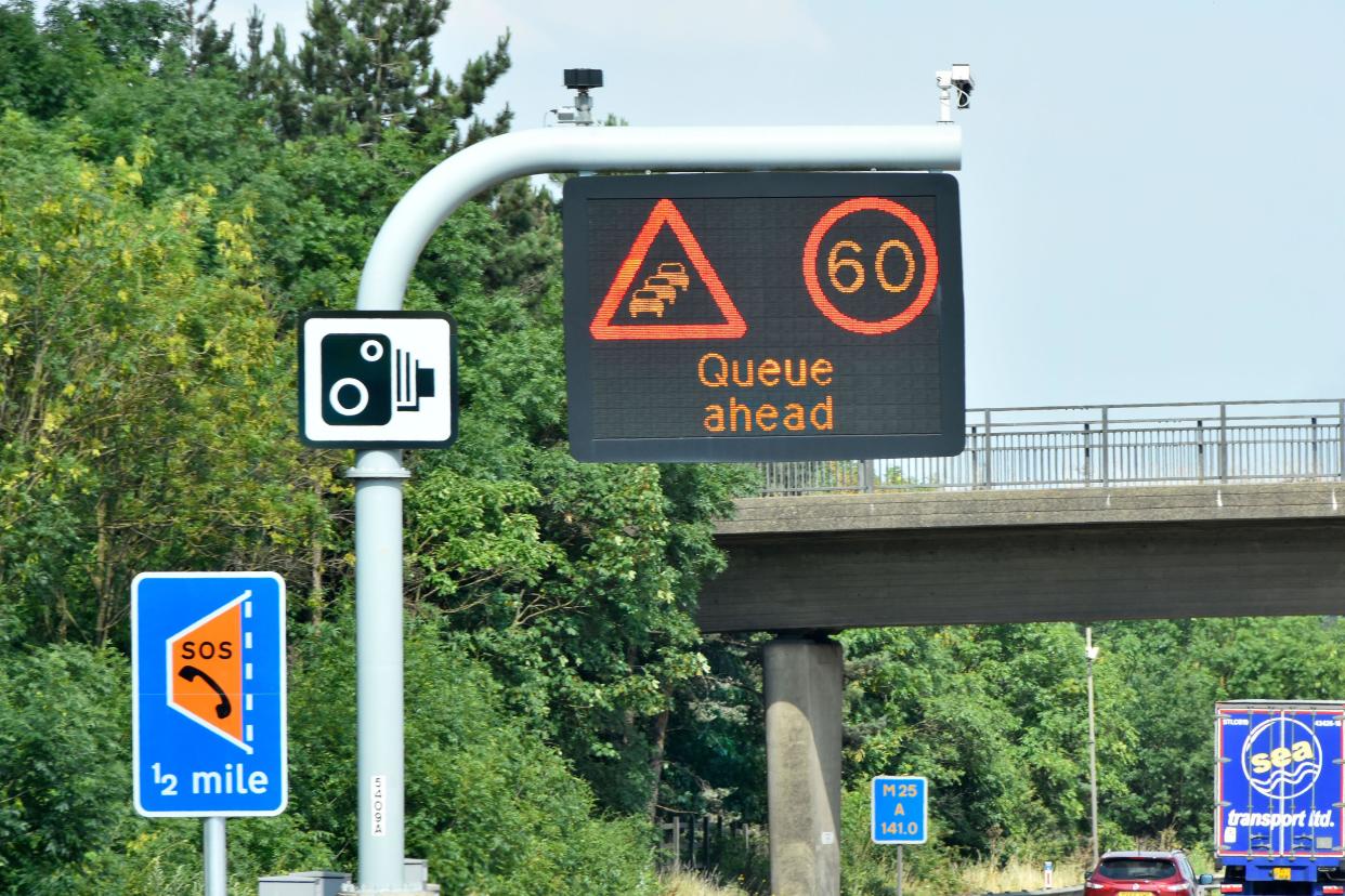 Single panel M25 motorway sign above lane one 60MPH variable speed limit & Queue Ahead message & smart lane layby half mile & standard camera signs UK