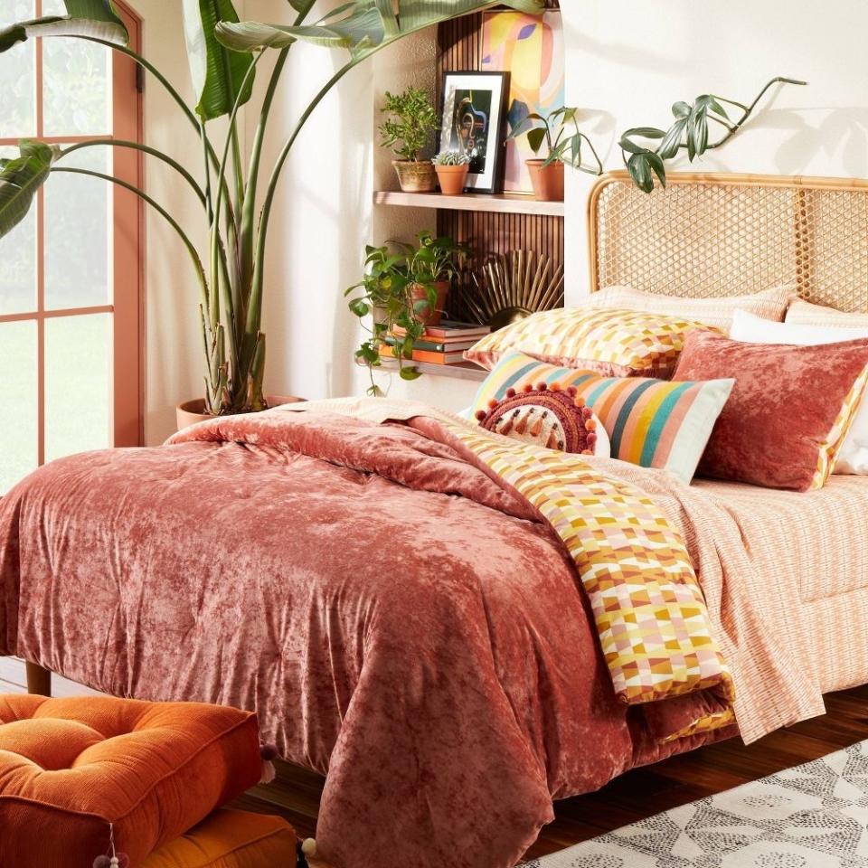 A cozy bedroom with a plush bed set and various decorative pillows, and plants in the background