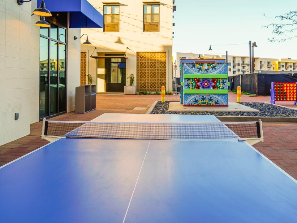 Culdesac Tempe: A blue ping pong table in a red-brick courtyard surrounded by white buildings