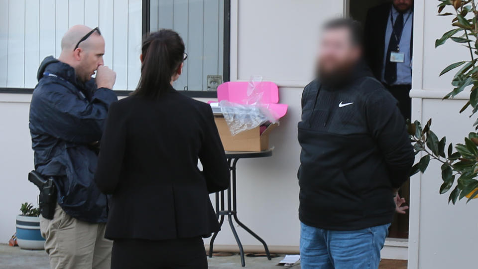 Two NSW Police detectives standing with handcuffed fake tax agent.