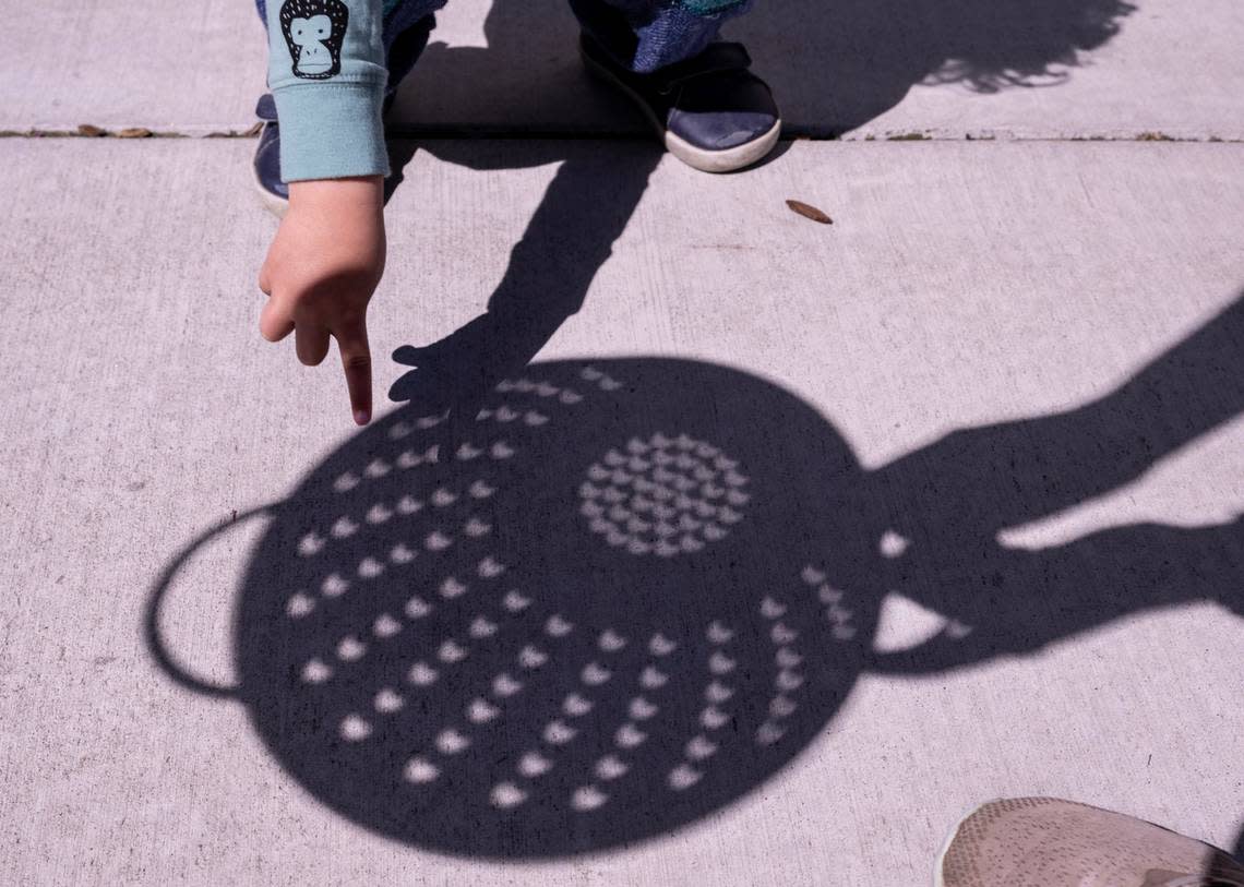 Wally Harrell, 3, looks at the crescent-shaped shadow of the solar eclipse as his mother Caroline holds a colander at Museum of Science and Curiosity in Sacramento on Monday, April 8, 2024.