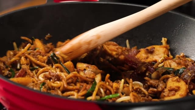 Frying char kway teow in pan with wooden spatula