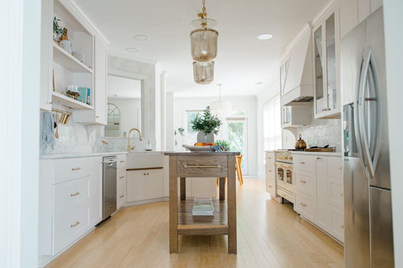 White remodeled kitchen with light wood floors, tiled backsplash and brass accents