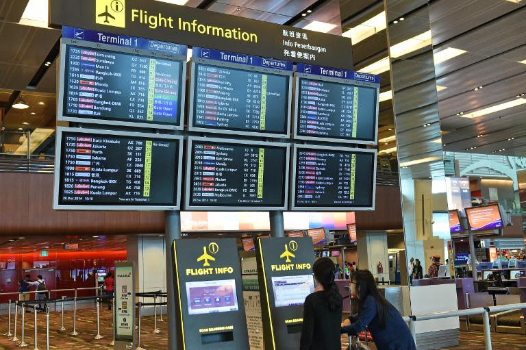 Passengers check flight information display boards at Singapore Changi airport terminal on December 28, 2014