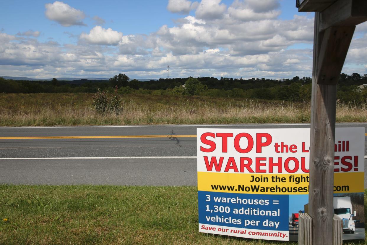 A road sign reading: "Stop the Lowhill warehouses" is on the side of the road, facing a large open field.