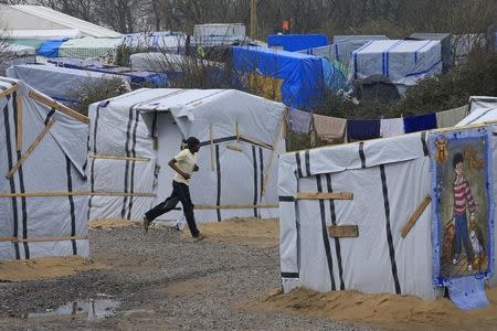 A migrant runs past makeshift shelters in the southern part of a camp for migrants called the "jungle", in Calais, northern France, February 26, 2016. REUTERS/Pascal Rossignol