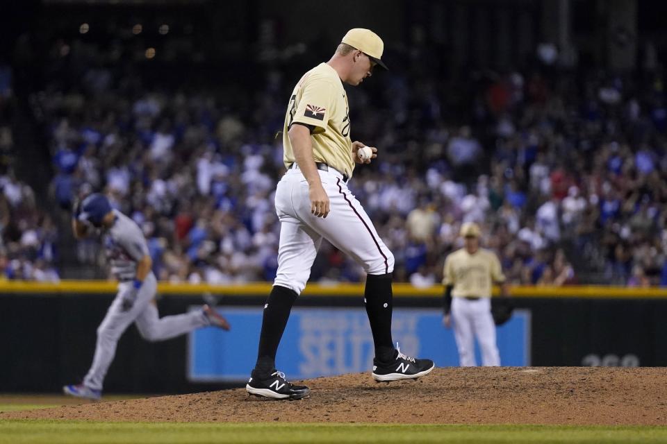 Arizona Diamondbacks relief pitcher Joe Mantiply pauses on the mound with a new baseball after giving up a home run to Los Angeles Dodgers' Steven Souza, left, as Diamondbacks shortstop Nick Ahmed, right, waits for the next batter during the eighth inning of a baseball game Friday, June 18, 2021, in Phoenix. (AP Photo/Ross D. Franklin)