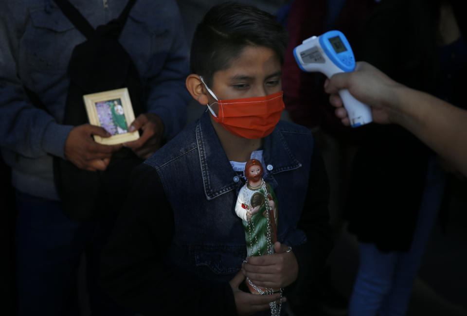 A boy holding a statue of Saint Jude and wearing a protective face mask amid the new coronavirus, stands still as his temperature is measured before entering the San Hipolito Catholic church, during the annual pilgrimage honoring Jude, the patron saint of lost causes, in Mexico City, Wednesday, Oct. 28, 2020. Thousands of Mexicans did not miss this year to mark St. Jude's feast day, but the pandemic caused Masses to be canceled and the rivers of people of other years were replaced by orderly lines of masked worshipers waiting their turn for a blessing. (AP Photo/Marco Ugarte)