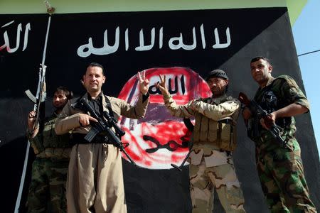 Kurdish Peshmerga fighters pose near a wall on which the black flag commonly used by Islamic State militants has been painted over, in the northern Iraqi town of Zumar, October 26, 2014, after having taken it from Islamic State. REUTERS/Azad Lashkari