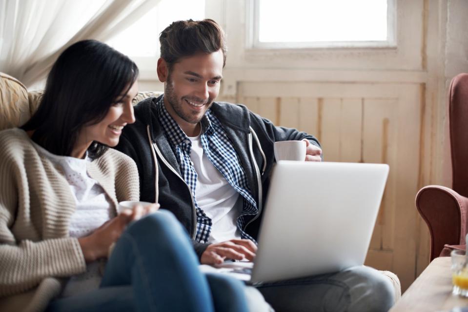 Two investors at home smiling while watching something on a laptop.