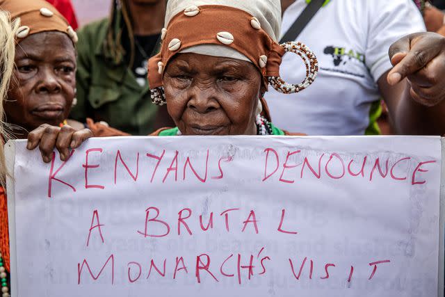 <p>LUIS TATO/AFP via Getty</p> A former freedom fighter holds a sign during a demonstration against the visit of King Charles to Kenya on October 30, 2023