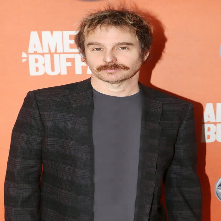 Sam Rockwell in a suit jacket and t-shirt with a mustache