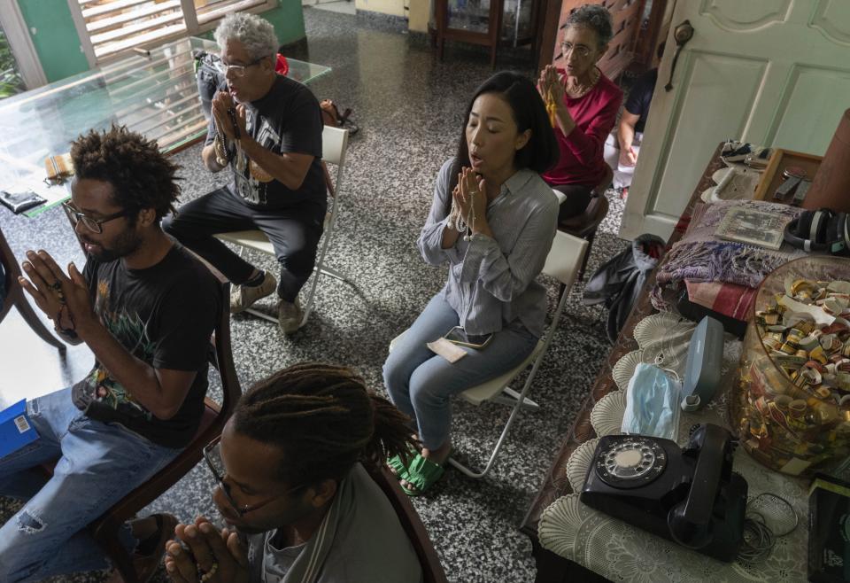 Los hermanos gemelos Yasnel y Yasmel Quintana, abajo a la izquierda, meditan en la casa del jazzista cubano César López, atrás a la izquierda, y su esposa Seiko Ishii, derecha al centro, el domingo 4 de febrero de 2024, en La Habana, Cuba. Hace diez años, los gemelos Quintana --que fueron criados en una familia afrocubana que sigue a la santería-- se unieron a la rama local de Soka Gakkai, una organización budista japonesa de alcance global. (AP Foto/Ramón Espinosa)