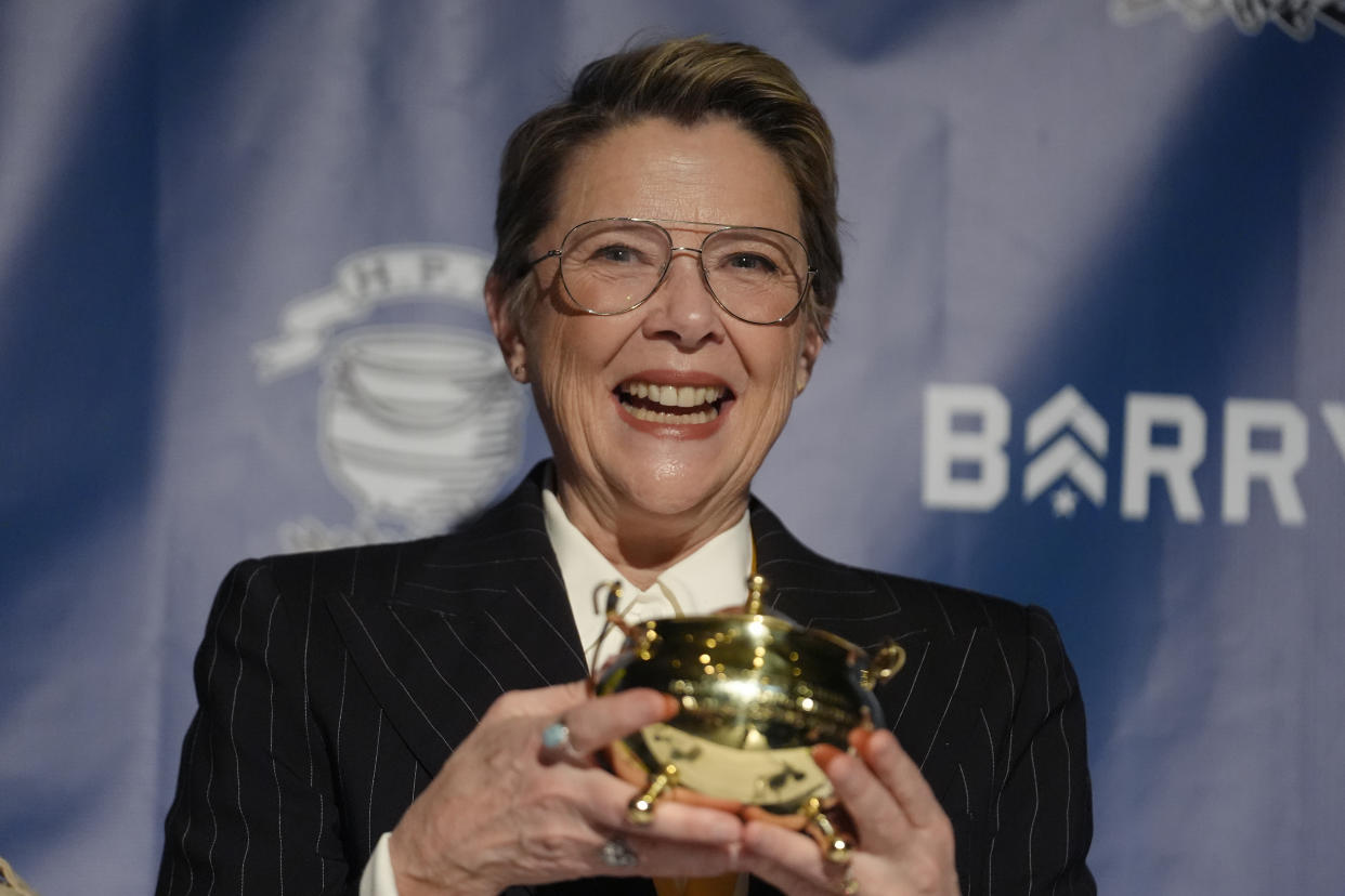 Actress Annette Bening holding a small gold award in the shape of a small pot.