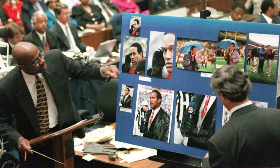 christopher darden points to a board with photos of oj simpson, he wears a suit and tie with a white collared shirt and glasses