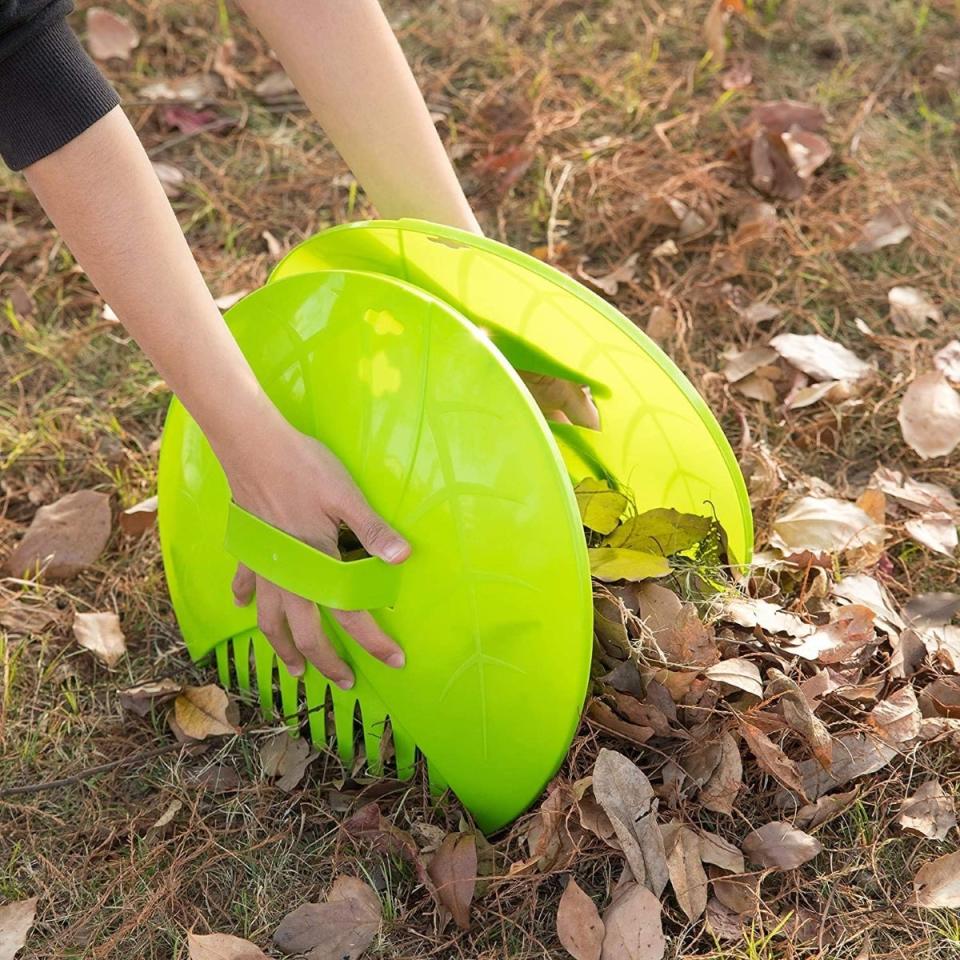 Using a pair of lime green leaf scoops to remove leaves from a lawn.