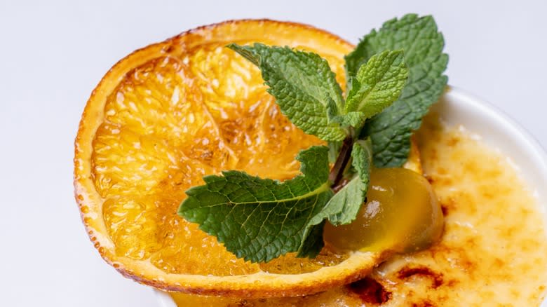 A creme brûlée garnished with mint sprig and a brûléed orange slice