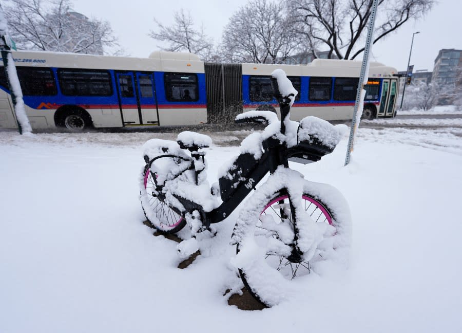 A bicycle sits covered with snow as a city bus moves along the westbound lanes of Speer Boulevard as a late winter storm dropped up to a foot of snow Thursday, March 14, 2024, in Denver. Forecasters predict that the storm will persist until early Friday, snarling traffic along Colorado’s Front Range communities. (AP Photo/David Zalubowski)