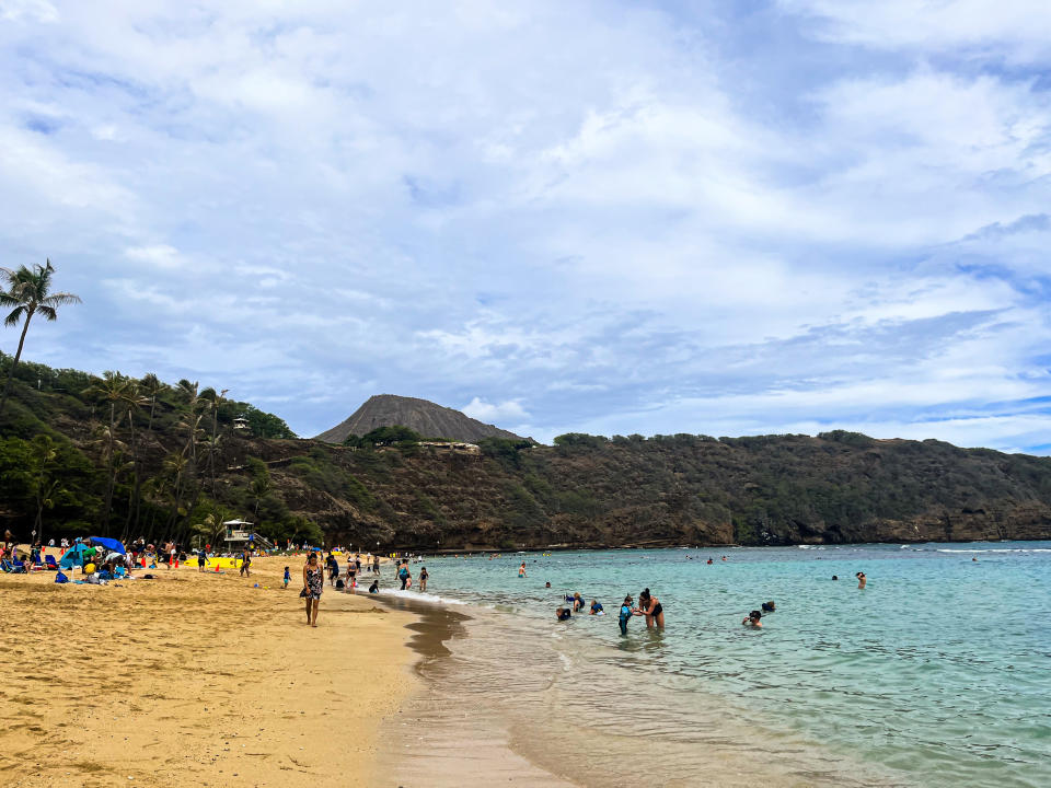 Beachgoers at a sandy beach with a mountain in the background and scattered clouds above