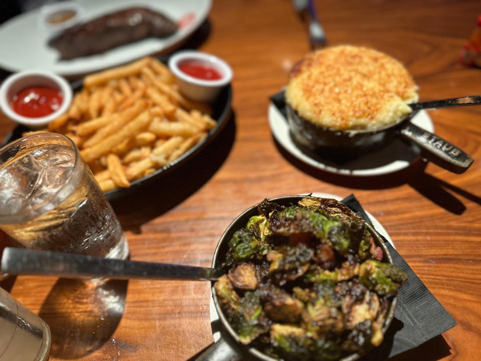 Roasted Brussels sprouts,  mashed potatoes, and a plate of fries with cups of ketchup on the plate