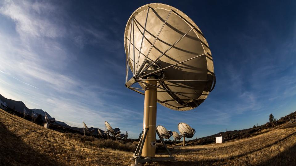     Large antenna dishes point up to the sky in a desert. 