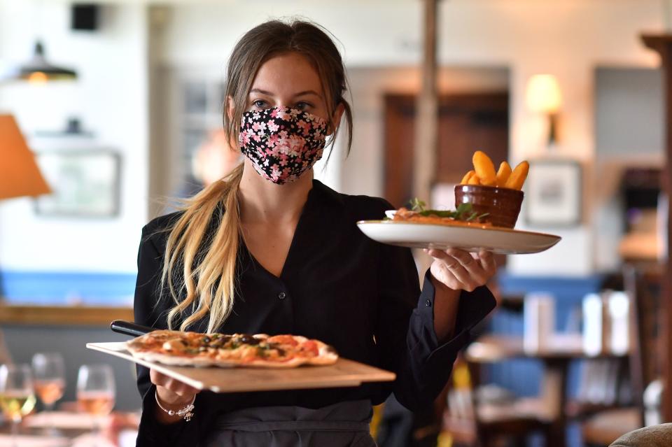 A staff member wears a face mask as she serves customers at the The Shy Horse pub and restaurant in Chessington, Greater London on July 4, 2020, on the first day of a major relaxation of lockdown restrictions during the novel coronavirus COVID-19 pandemic. Credit: Getty.