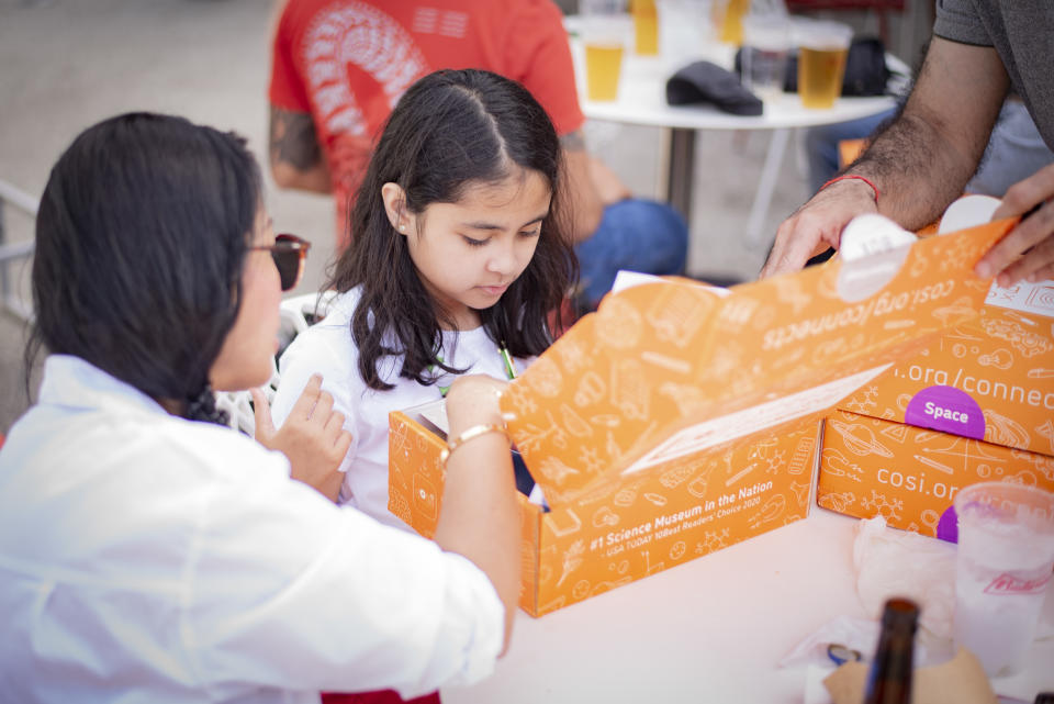 child looks into an open box. a parent gestures to the child and the box on the left