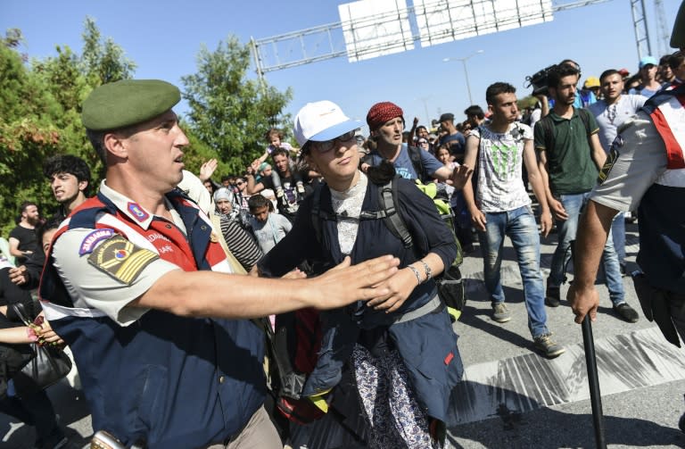 A Turkish police officer gestures to colleagues as Syrian migrants and refugees march along the highway towards the Turkish-Greek border at Edirne on September 18, 2015