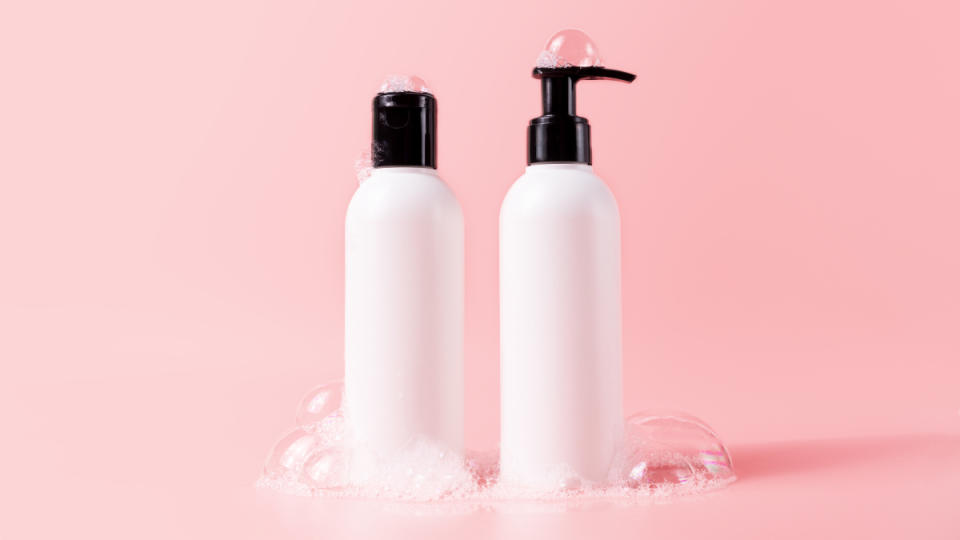 White shampoo and conditioner bottles against a pink background