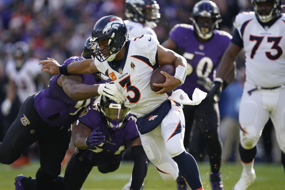 Denver Broncos quarterback Russell Wilson (3) scrambles under pressure from Baltimore Ravens defensive tackle Calais Campbell (93), left, and Baltimore Ravens linebacker Tyus Bowser (54), in the first half of an NFL football game, Sunday, Dec. 4, 2022, in Baltimore. (AP Photo/Patrick Semansky)