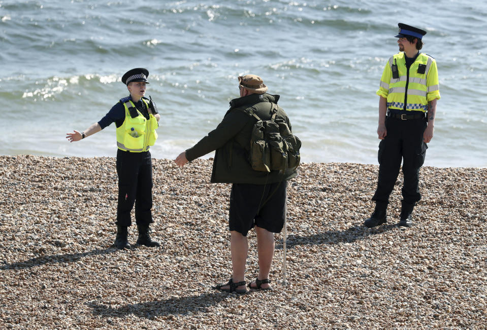 Police officers speak to a man as they patrol the beach in Brighton as the UK continues its lockdown to help curb the spread of coronavirus, in Brighton, England, Saturday April 25, 2020. (Gareth Fuller/PA via AP)